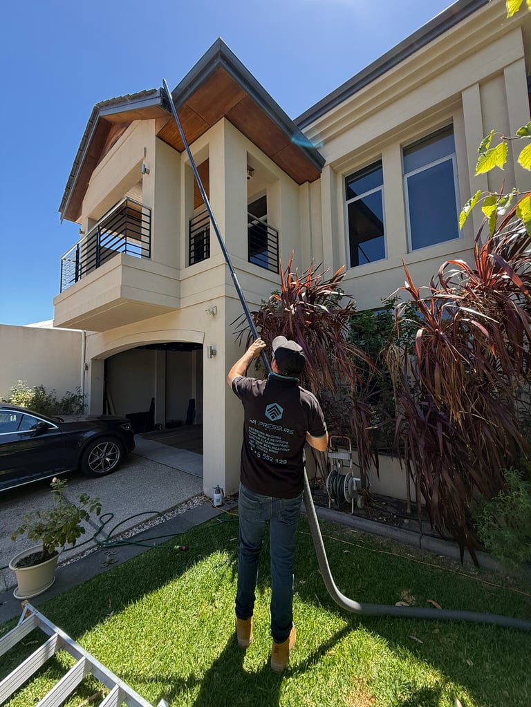 Worker cleaning brown palm fronds on modern two-story home with cream exterior and garage visible