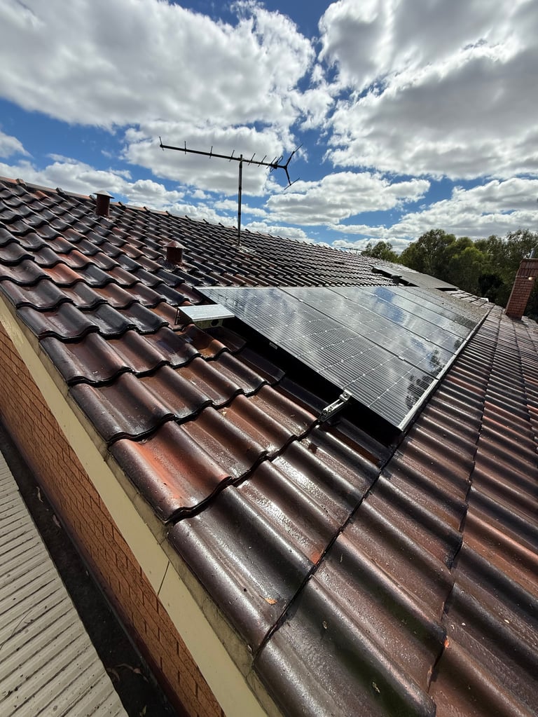 Solar panel and TV antenna mounted on a residential roof with dark tiles against a blue sky with white clouds