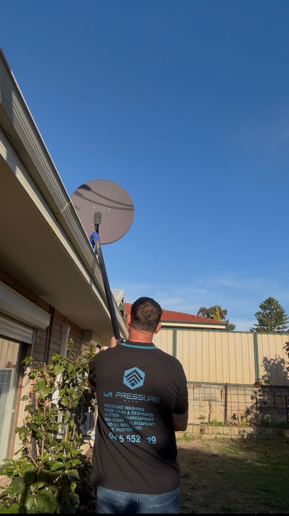 Technician installing a satellite dish on a residential house roof under clear blue sky